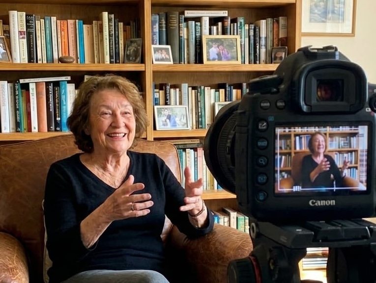 Woman being filmed telling her story in front of a bookshelf
